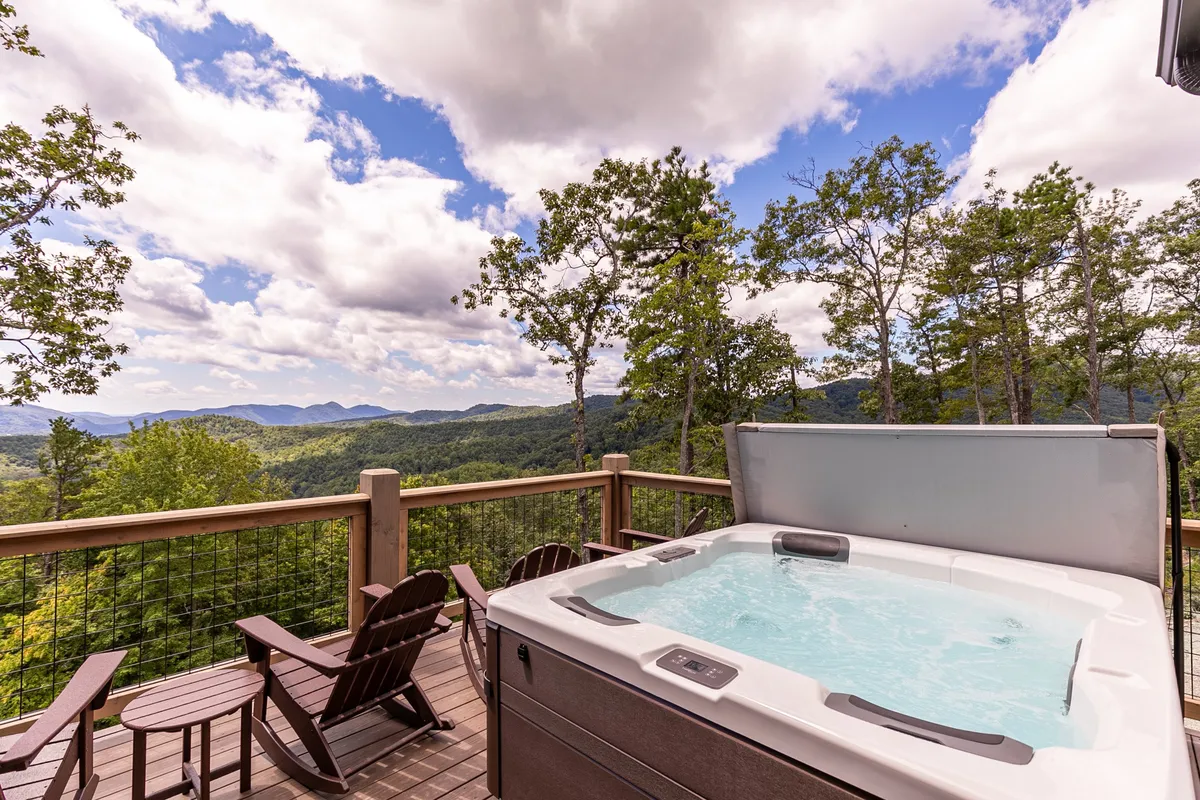 A serene wooden deck with a bubbling hot tub, adirondack chairs, and panoramic views of the Blue Ridge Mountains. The setting invites relaxation at sunset or under the stars, emphasizing the tranquil, retreat-like atmosphere.