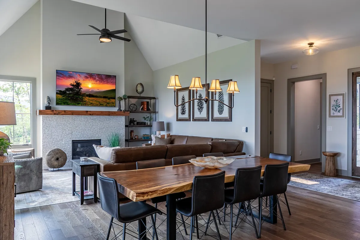 A warm and cozy great room shot showing a dining table, comfortable sofa seating area, modern fireplace, TV, and an elegant chandelier. The layout supports both dining and lounging, making it ideal for shared meals, movie nights, and informal socializing.