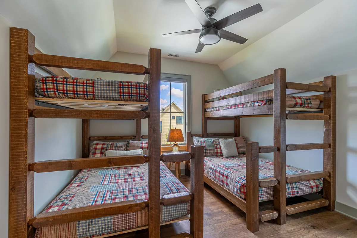 A cheerful bunk room featuring twin-over-full bunk beds, a window view, and a warm lamp. The space feels friendly and communal, perfect for kids or guests to unwind, read, or share stories.