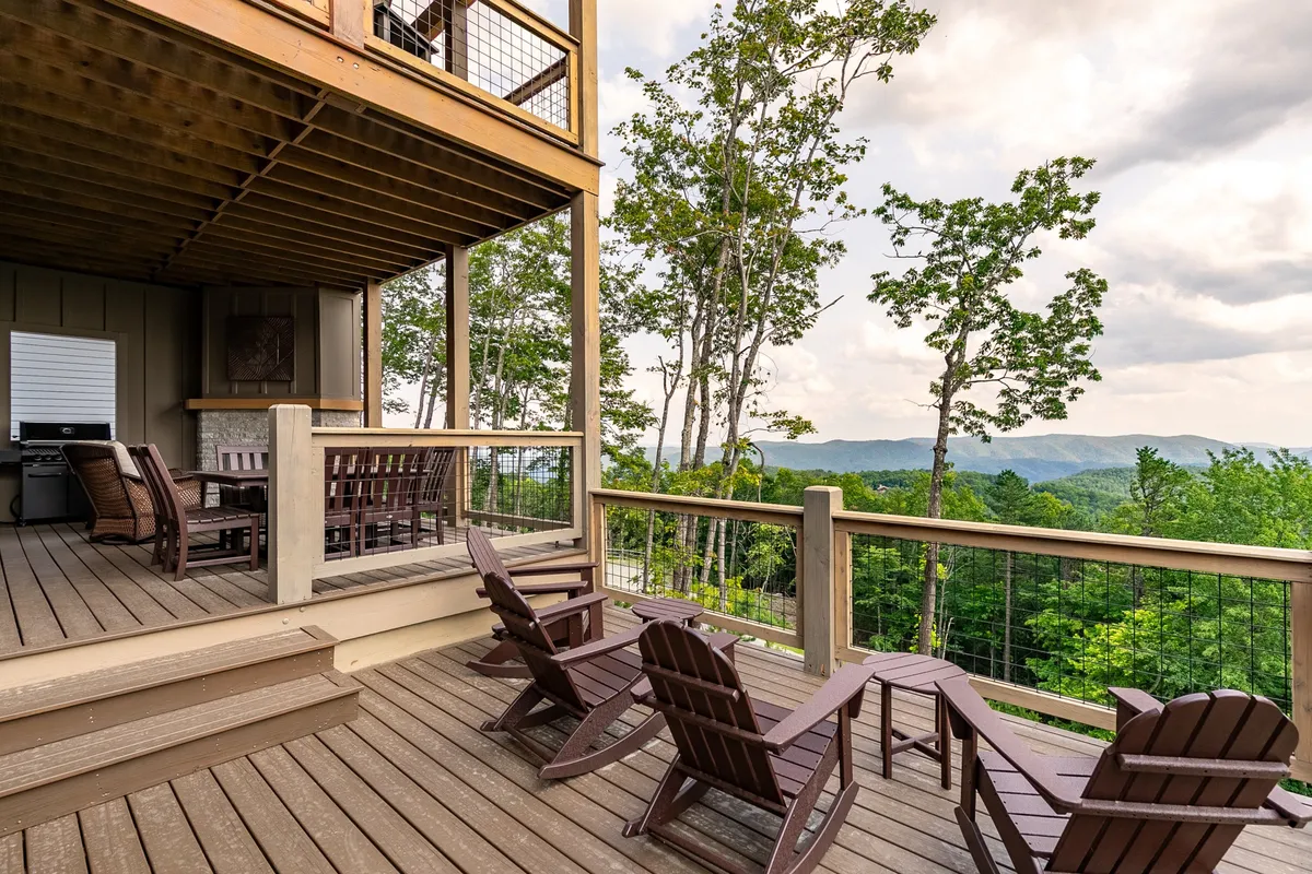 A relaxed exterior view of a deck furnished with comfortable chairs and a dining table, surrounded by trees and offering unobstructed views of the mountains. The space is ideal for outdoor dining, meditation, yoga stretches at sunrise, or simply enjoying the fresh mountain air in a communal setting.