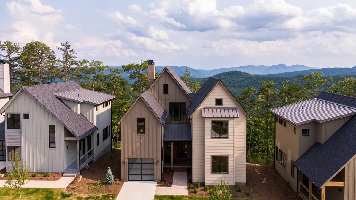 The image showcases a beautifully designed modern single-family house nestled in the Blue Ridge mountains, with a landscaped front yard, an inviting driveway, and sweeping views of the surrounding peaks. The warm glow of the sunset bathes the scene, creating a welcoming ambiance perfect for family gatherings and outdoor relaxation.