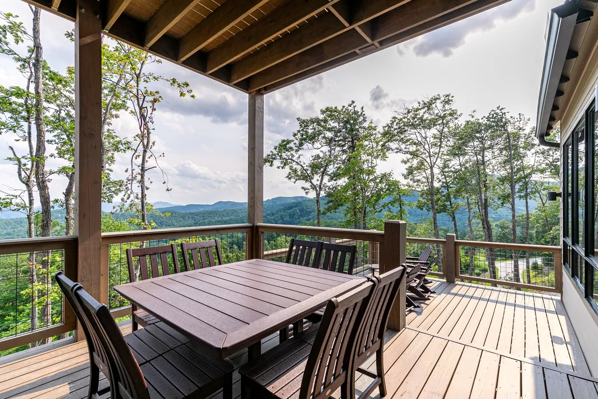 A peaceful outdoor dining area with a wooden table set against a backdrop of surrounding trees and mountain views. The scene is bathed in warm, golden light, suggesting sunset or early evening, and conveys the opportunities for communal gatherings and enjoying nature.