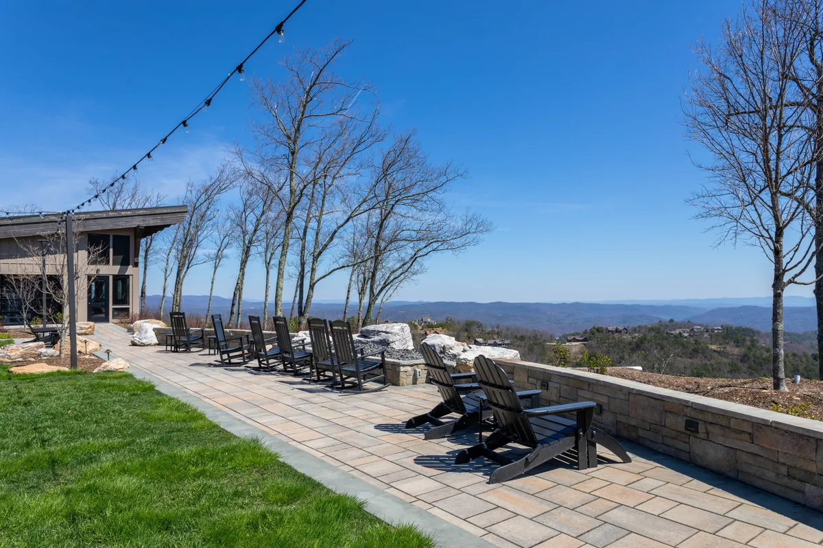 This exterior image features adirondack chairs arranged on a pathway, with panoramic mountain views and string lights overhead. The scene captures a sense of tranquility and connection with the stunning natural surroundings, inviting guests to relax and enjoy the scenery.