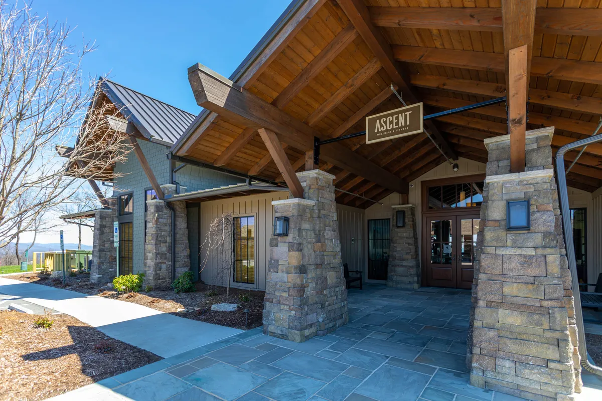 A welcoming exterior scene with wooden beams, stone columns, and an entrance sign, evoking the feeling of entering an exclusive, well-maintained community. The porch area and natural setting enhance the sense of security and belonging.