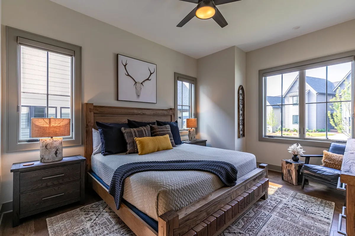 A tranquil bedroom featuring a plush bed with soft linens, matching nightstands, windows that let in natural light, and tasteful wall artwork. The setting offers a peaceful and inviting atmosphere ideal for restful sleep or quiet relaxation.
